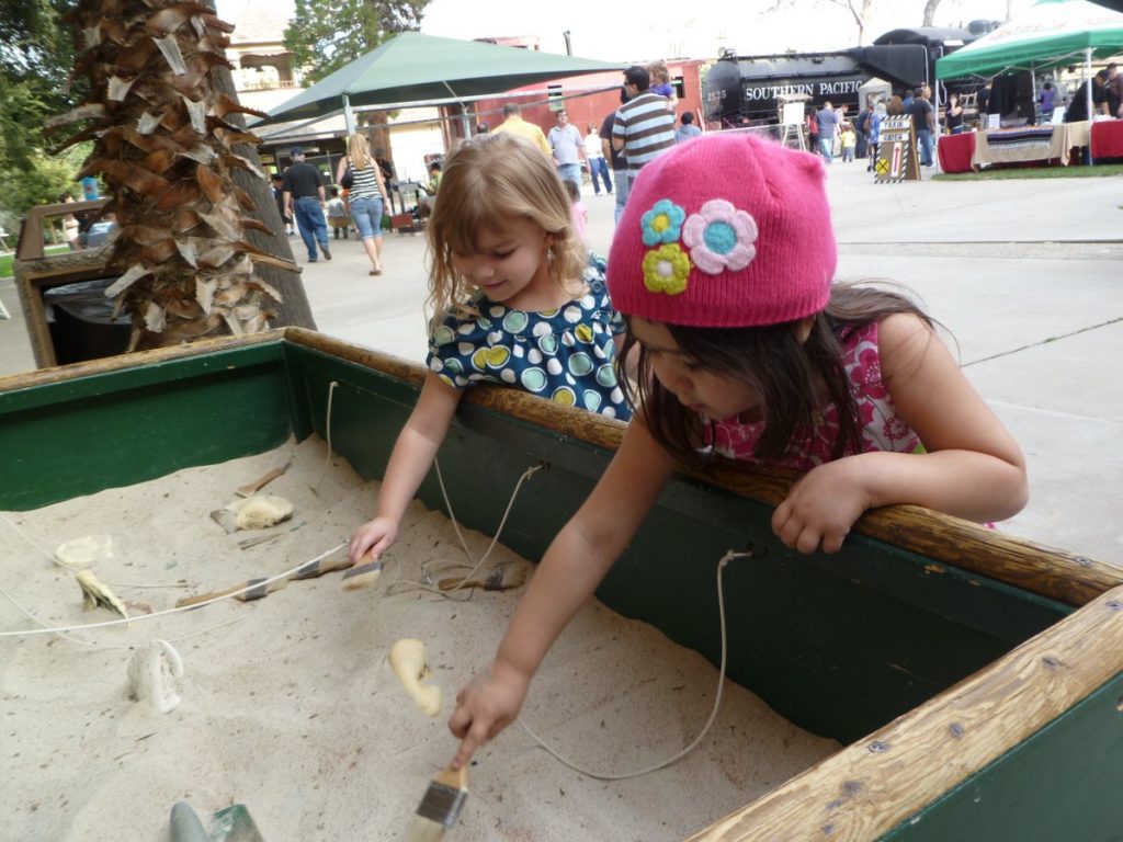 Children reaching into a interactive display box filled with sand and bones to mimic find a fossil at the museum.