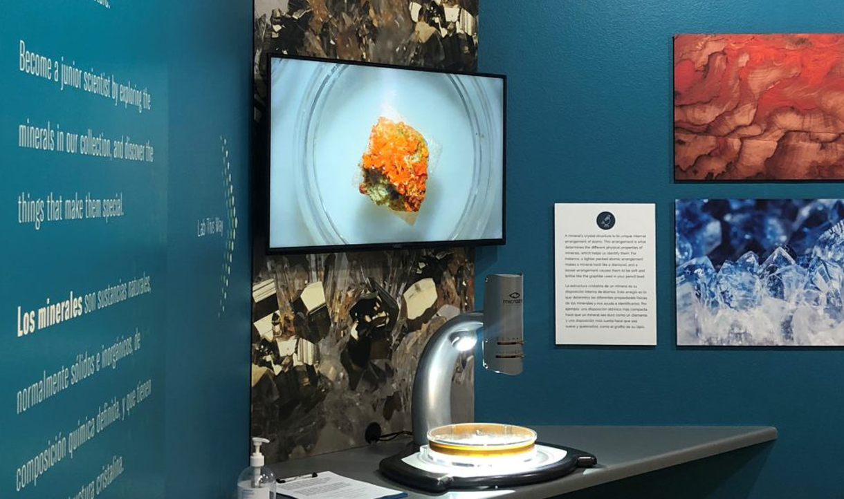 A wall display of minerals with a microscope of a mineral displayed on an enlarged monitor above it at the Victor Valley Museum.