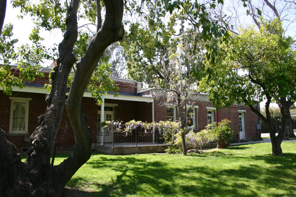 An outside view of the Maria Merced Williams and John Rains house seen in the background with green trees in the front and green grass.