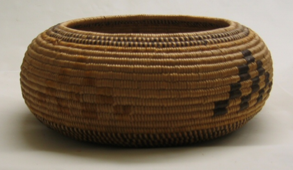 An old Indian handmade basket is seen with checkered patterns woven into the  design.