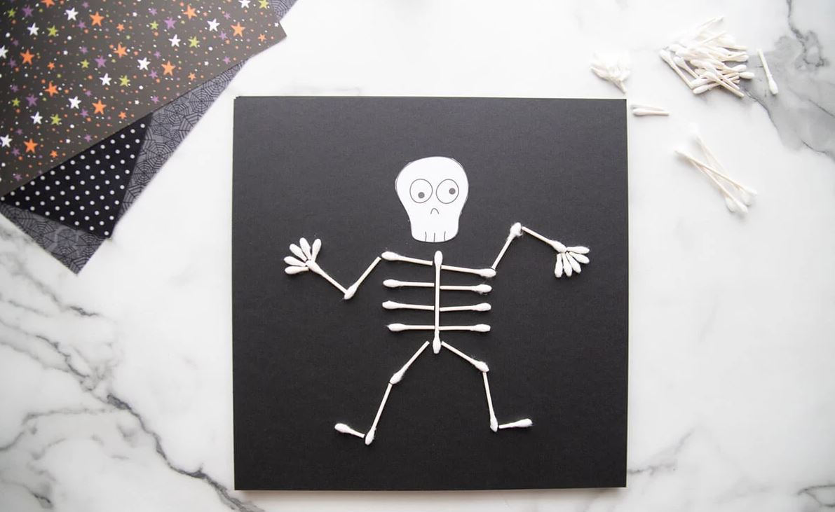 Q-TIp skeleton on a black piece of paper with extra craft materials in the background.