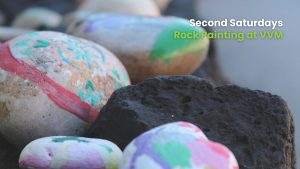 Close-up of several painted rocks, including one with red and green brushstrokes and others with pastel-colored designs, placed next to a dark porous volcanic rock.