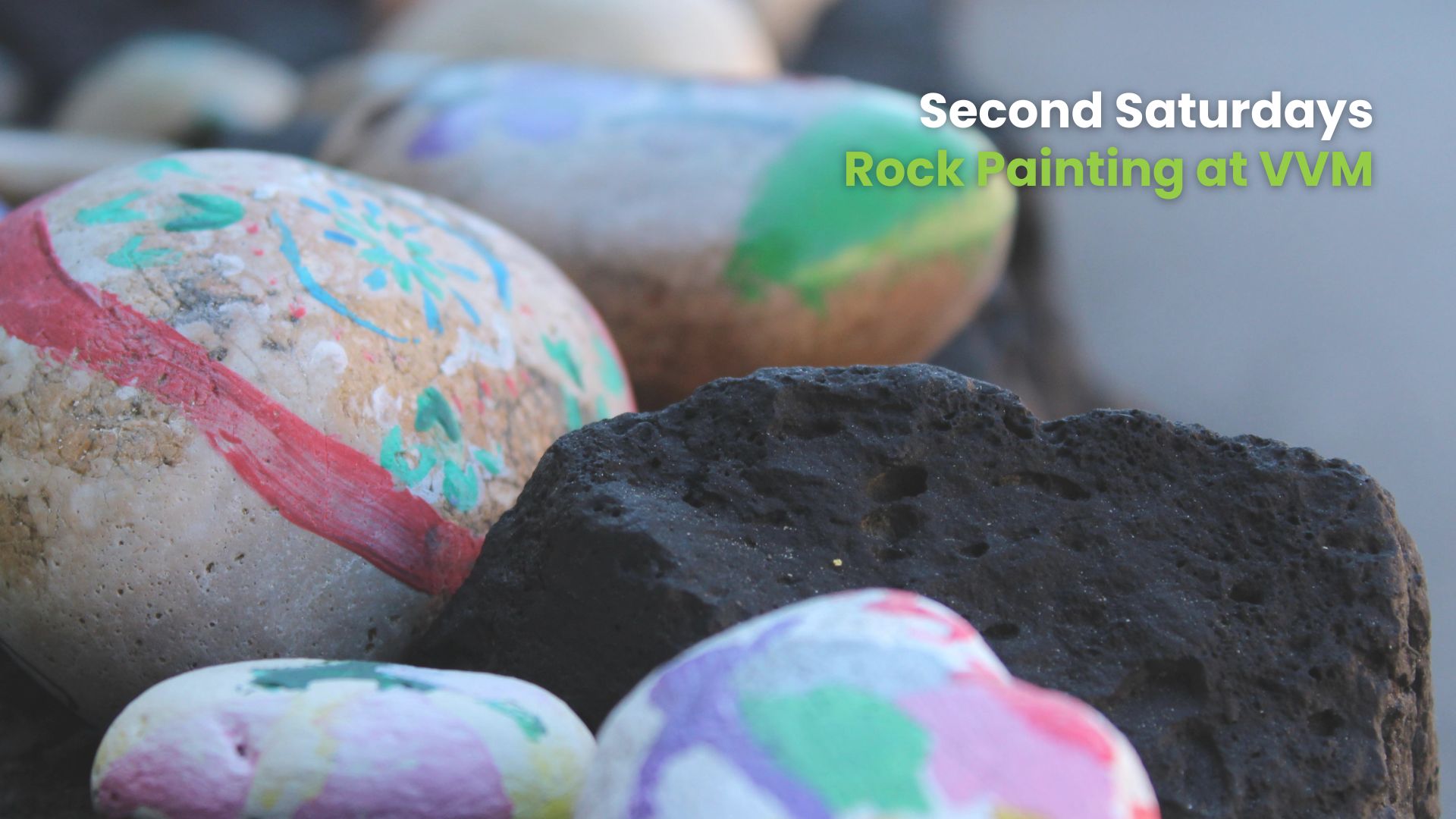 Close-up of several painted rocks, including one with red and green brushstrokes and others with pastel-colored designs, placed next to a dark porous volcanic rock.
