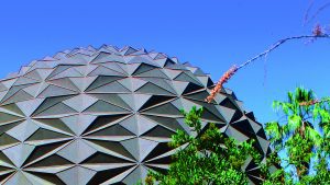 Geometric dome rising above desert plants and palm trees under a bright blue sky at Epcot in Walt Disney World.