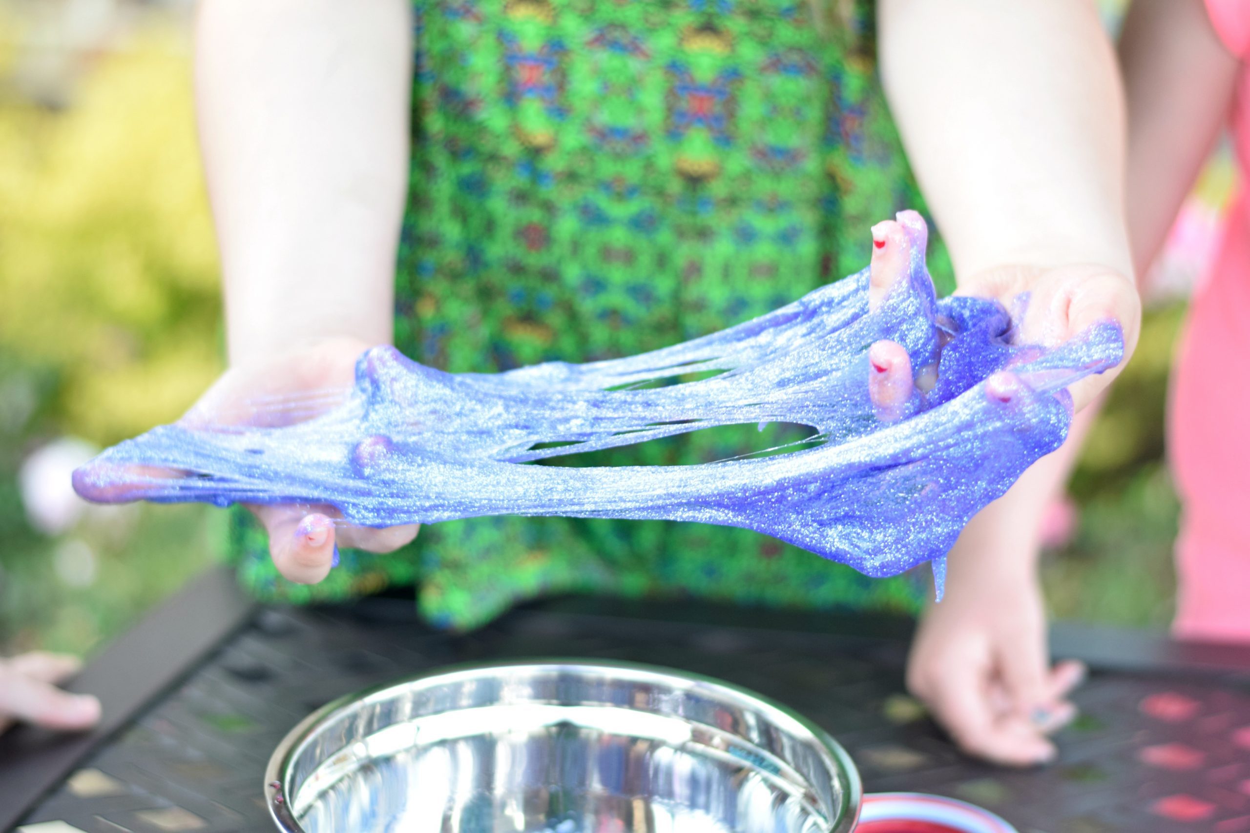 A girl holds blue and purple slime in her hand.